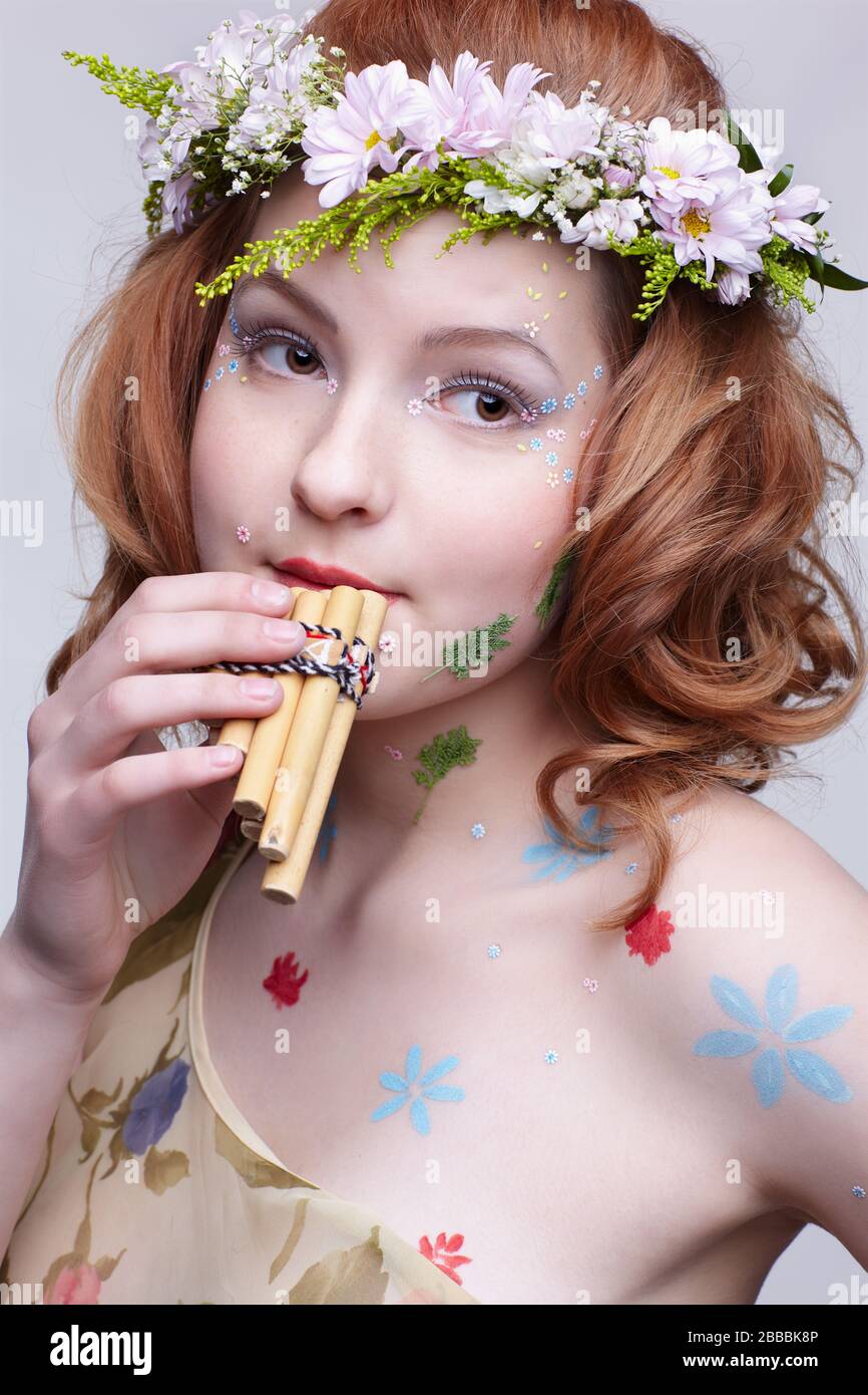 portrait of beautiful slavonic redhead girl in flower garland playing panflute Stock Photo