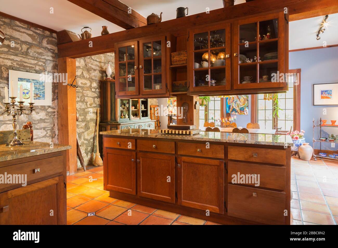 Stained wooden shaker style cabinets and nuanced granite countertops in kitchen with terracotta ceramic tile flooring inside an old circa 1830 Quebecois style country home, Quebec, Canada. This image is property released. CUPR0357 Stock Photo