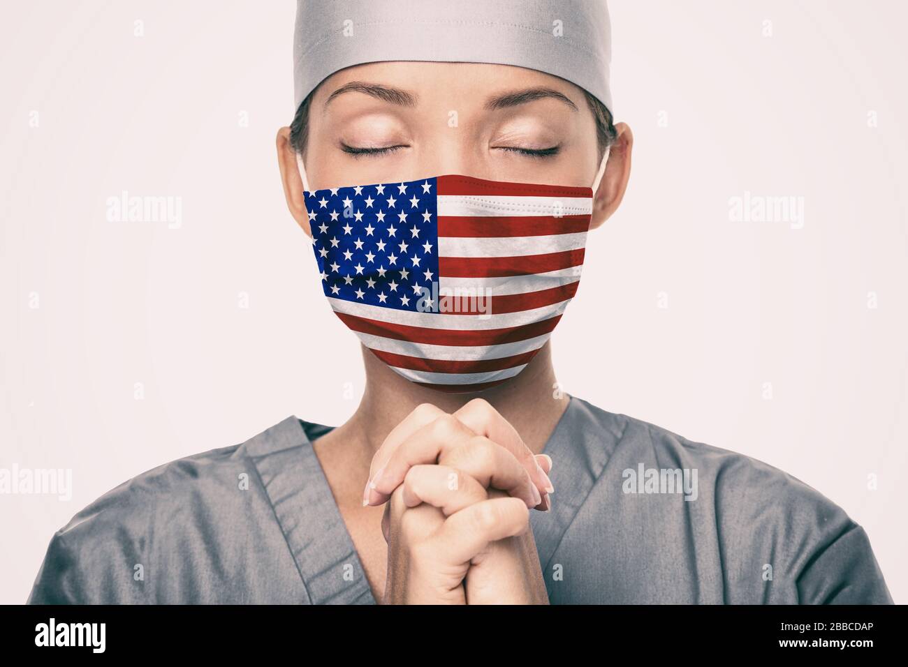 Coronavirus pandemic in the United States of America. USA american flag print on doctor's mask praying with claspeds hands in hope for help. Crying for help, disaster aid needed in the US. Stock Photo
