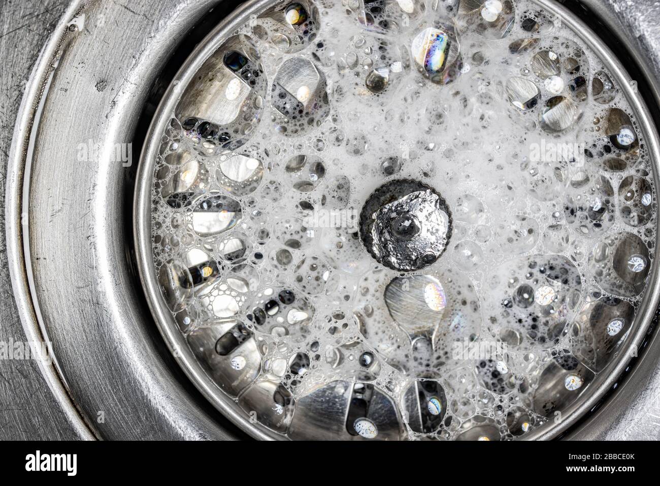 White foam with bubbles of cleaner in a washbasin, macro view. Drain