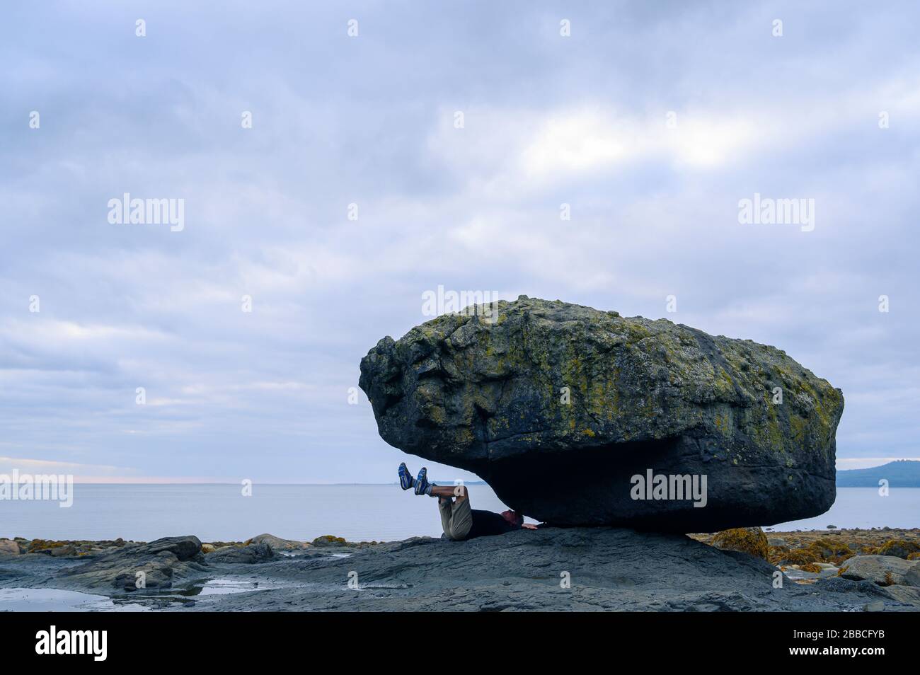 Man plays like being trapped inder Balance Rock, Skidegate, Haida Gwaii, Formerly known as Queen Charlotte Islands, British Columbia, Canada Stock Photo