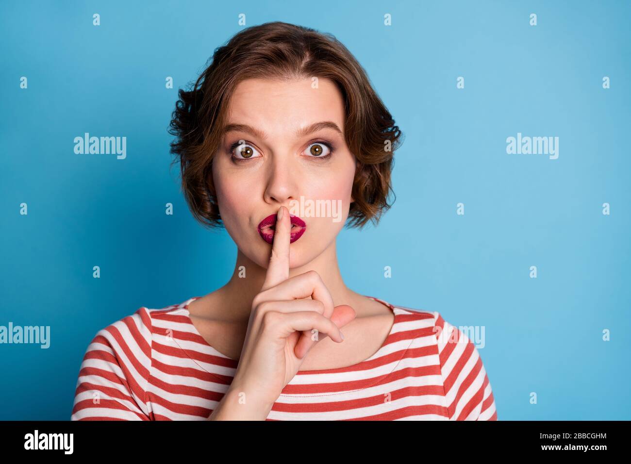 Hush please. Closeup photo of beautiful pretty lady hold index finger on lips asking colleagues keep silence wear casual red white shirt isolated blue Stock Photo