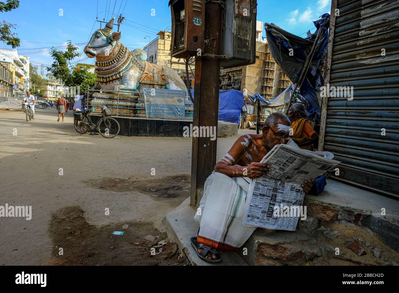 Madurai, India - March 2020: A man reading the newspaper next to the blue Nandi in front of the entrance to the Pudhu Mandapa on March 10, 2020 in Mad Stock Photo