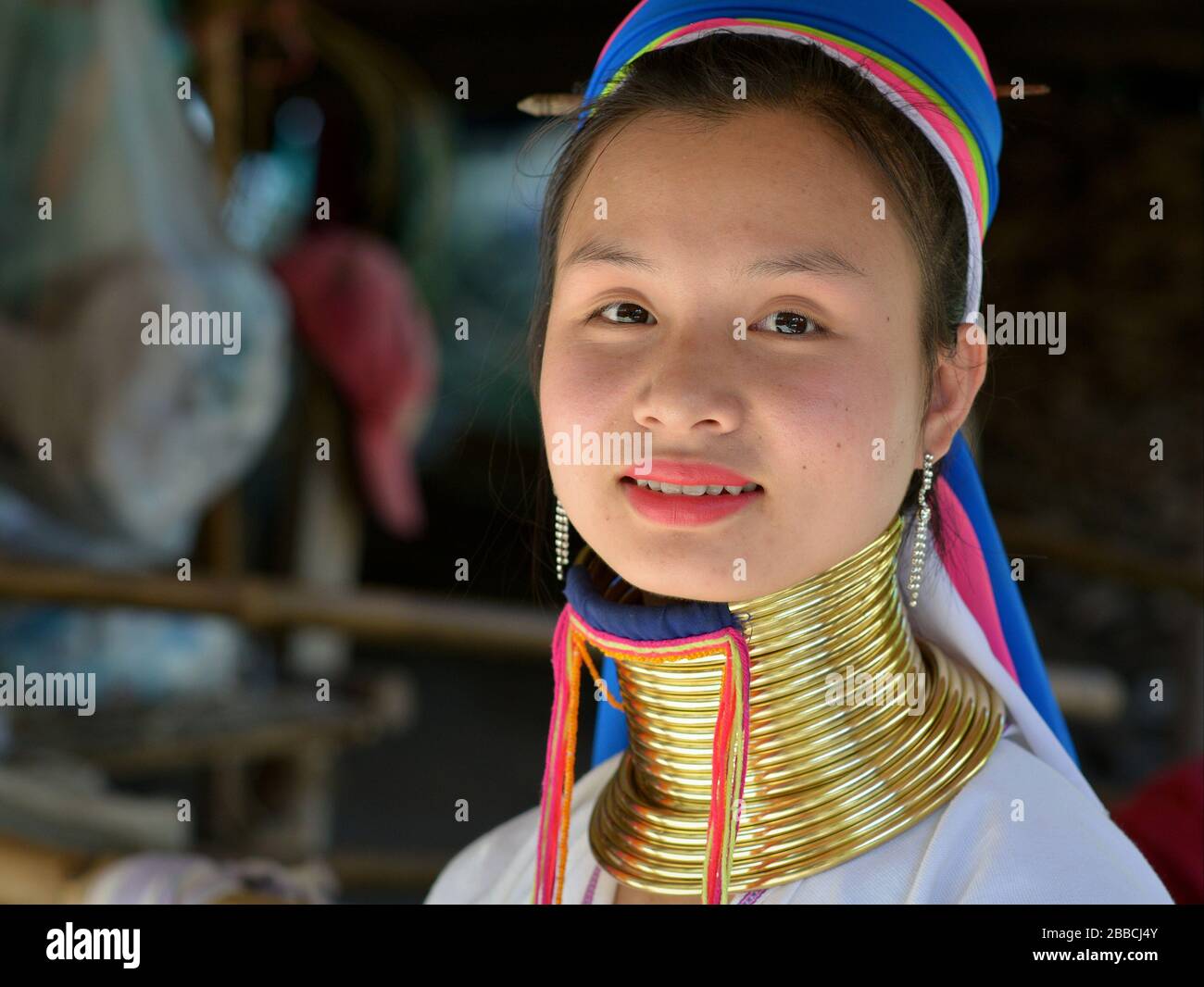 Pretty Thai/Burmese long-neck Kayan teen girl (“giraffe woman”) with polished tribal Padaung brass neck rings/coils smiles for the camera. Stock Photo