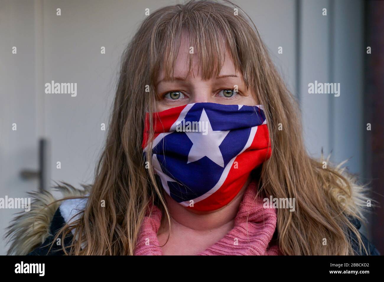 A 40 year old blonde woman is wearing a fabric mask. It protects against Corona Virus. Homemade mask made of fabric with stars and stripes. Stock Photo