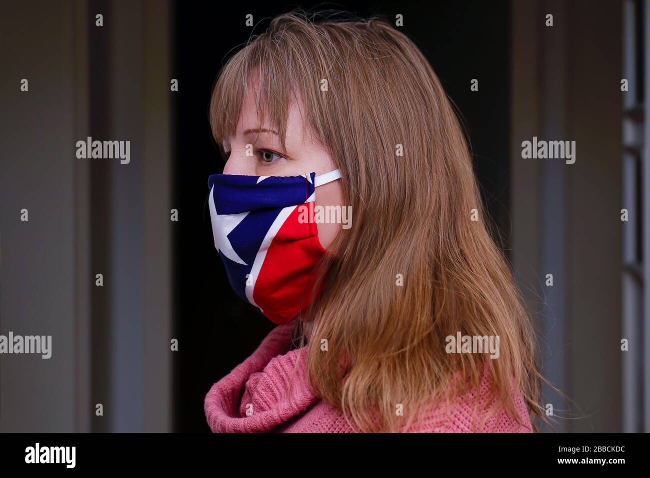 A 40 year old blonde woman is wearing a fabric mask. It protects against Corona Virus. Homemade mask made of fabric with stars and stripes. Stock Photo