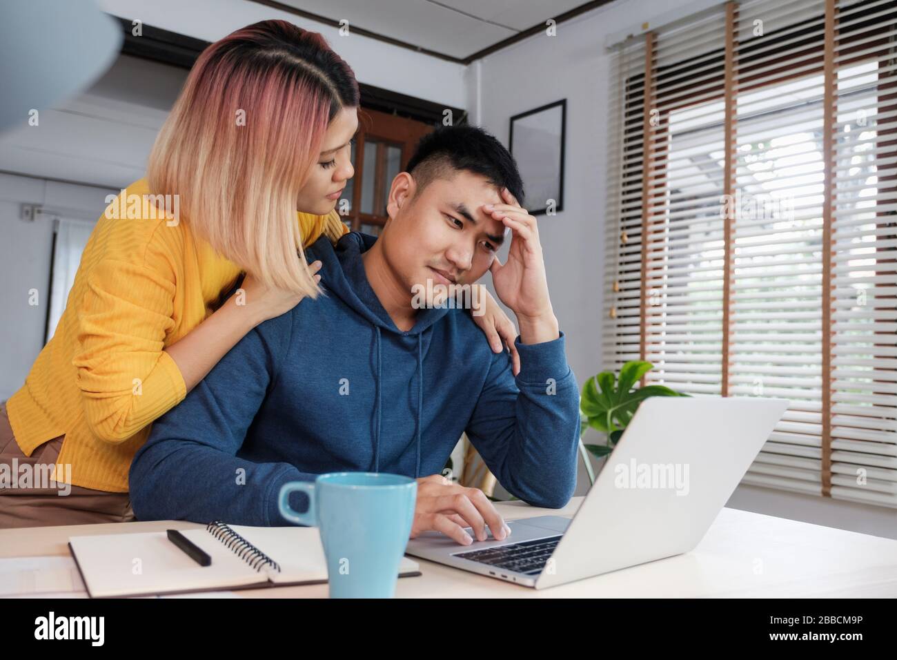 Asian female girlfriend encouragement boyfriend from stress while working on home budget on laptop at living room in home Stock Photo