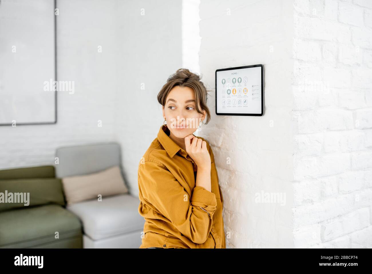 Portrait of a happy young woman controlling home with a digital touch screen panel installed on the wall in the living room Stock Photo