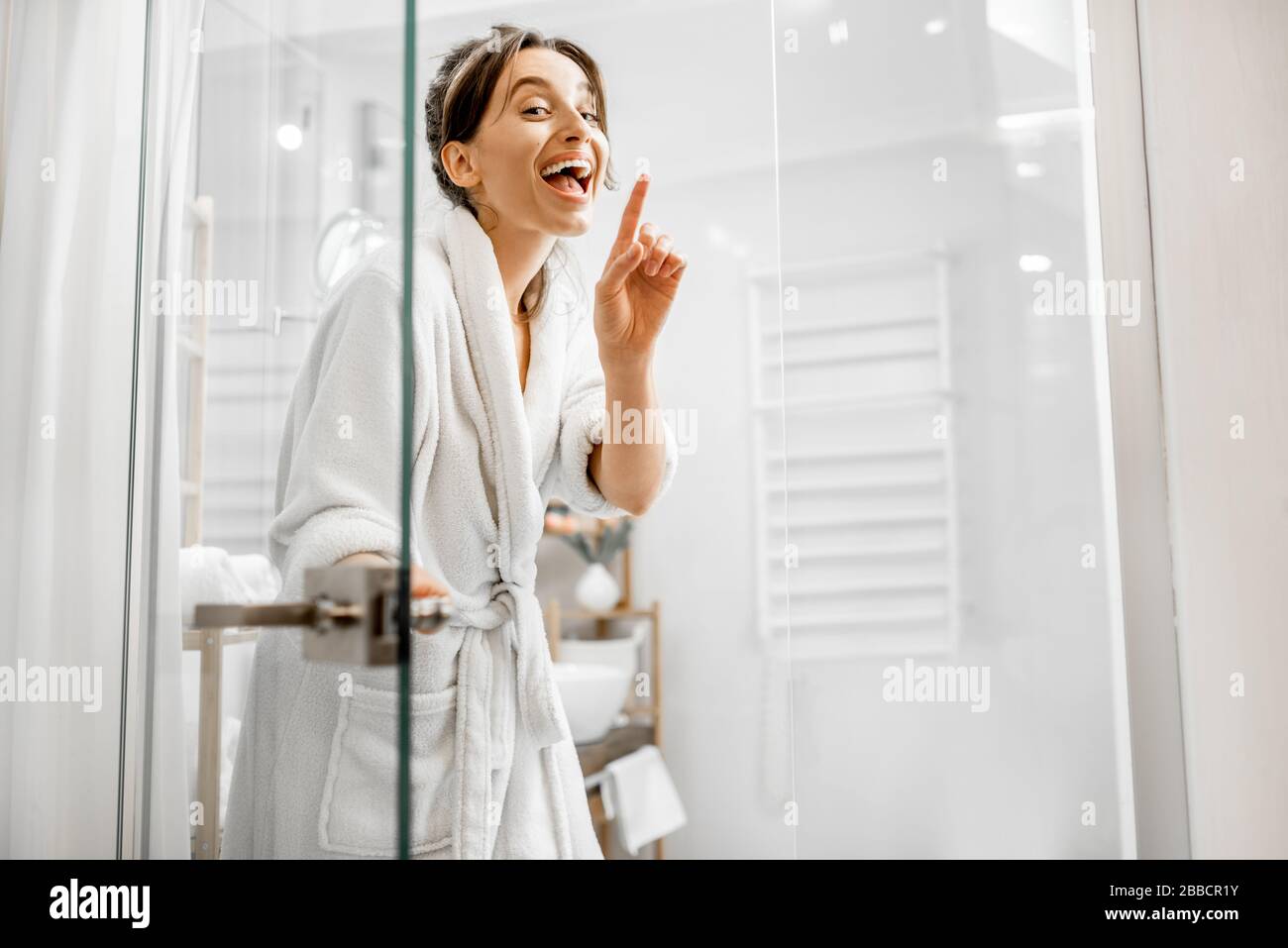 Young and joyful woman in bathrobe going to the bath, closing a glass doors at home Stock Photo