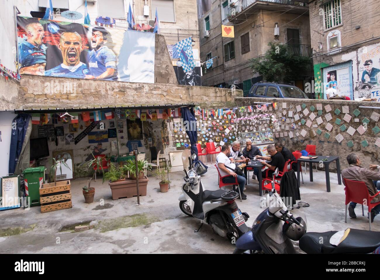 People playing cards in the Spanish Quarter of Naples under a poster of Napoli football club's players Stock Photo