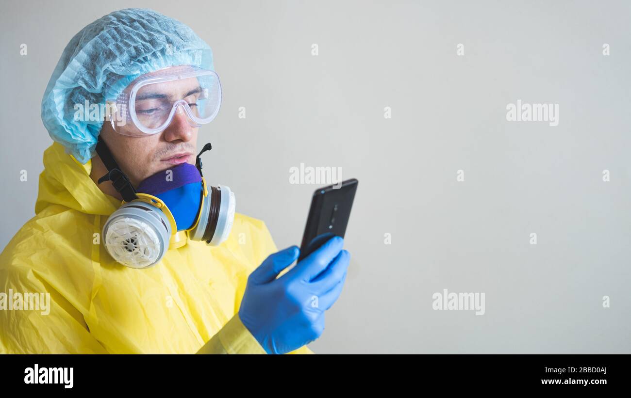 Medical worker in protective gear using smartphone after a shift. Concept of covid-19 epidemic, healthcare personell and overworking in hospitals. Stock Photo