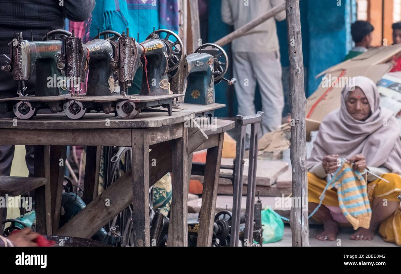 Old Indian woman sitting in front of a sewing machine repair shop knitting Stock Photo