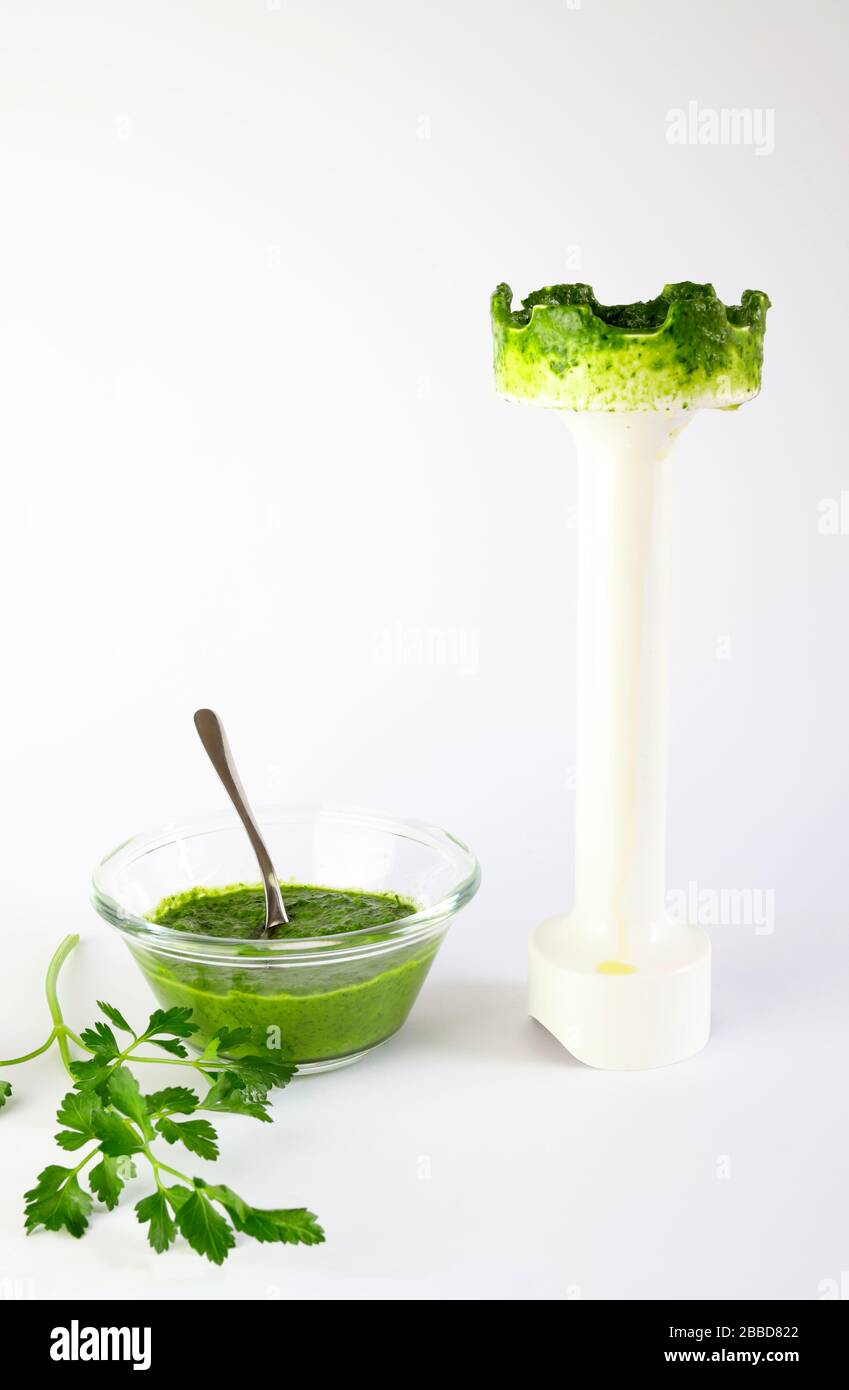Closeup of a bowl with parsley sauce and a hand blender immersed in the