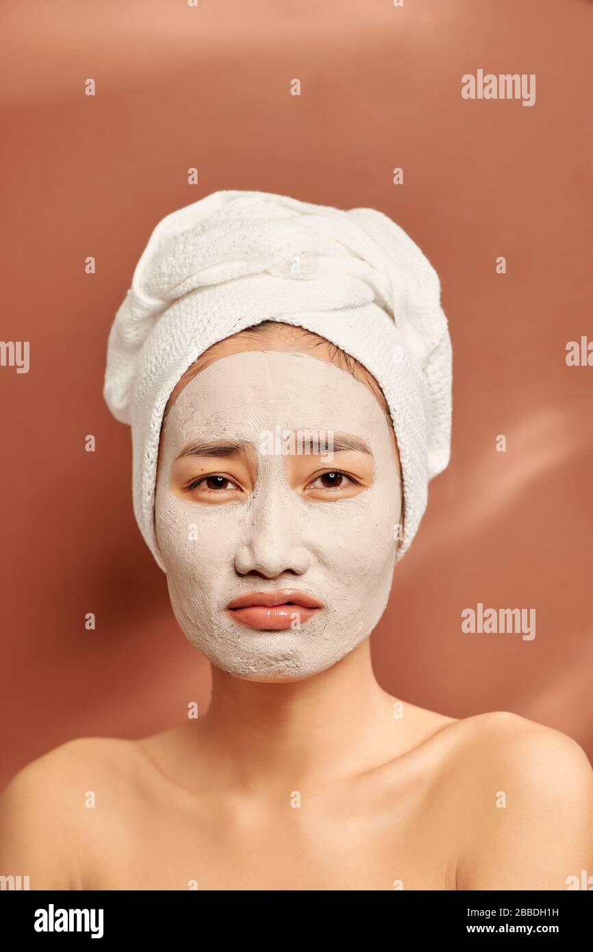 Beautiful cheerful Asian teen girl applying facial clay mask. Beauty treatments, isolated on light background. Stock Photo