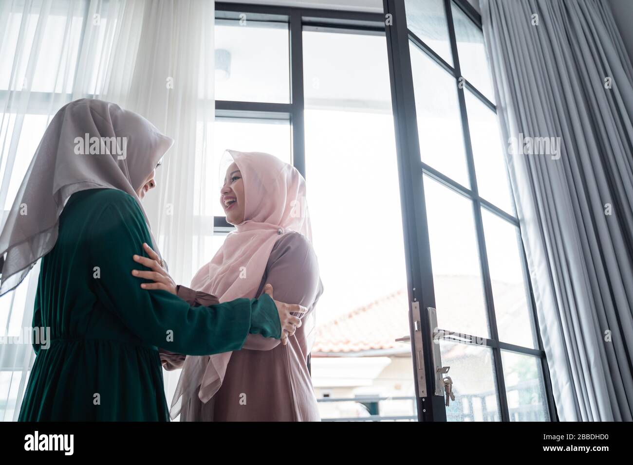 muslim hijab woman happily entrace home opens the door and meets her sister Stock Photo