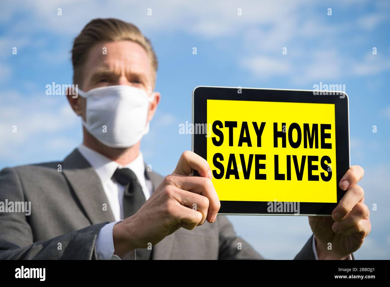 Businessman wearing COVID-19 protective face mask holding a tablet with a Stay Home, Save Lives message Stock Photo