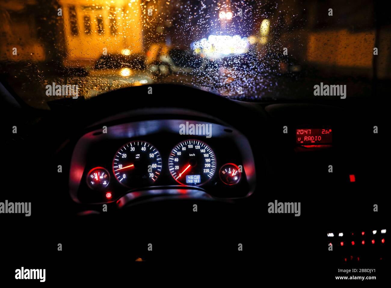 Shallow depth of field image (selective focus) with the steering wheel and dashboard lights of a 2010 car and the windscreen with drops of rain. Stock Photo