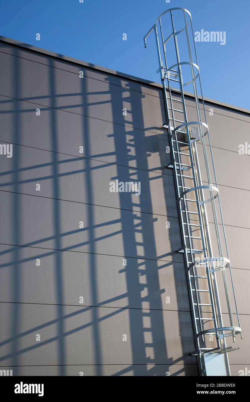 Fire escape or rescue ladder at a modern industrial building with shadows on the wall Stock Photo