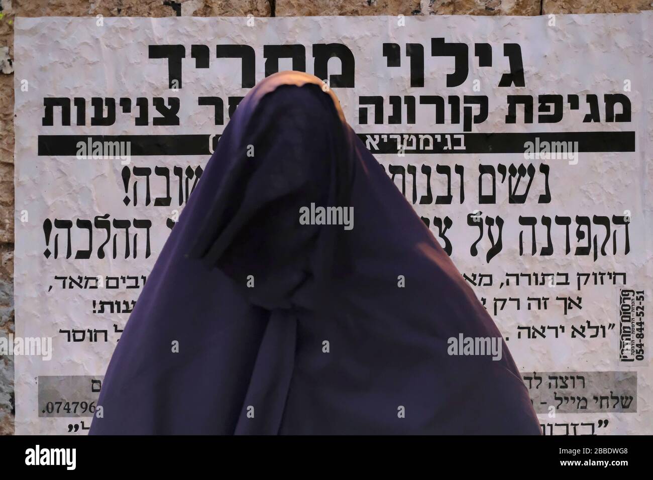 A woman of the so called Haredi Burqa Sect ( Jewish religious group, in which ultra-Orthodox Jewish women claim that modesty calls for a burqa-style covering of the entire body ) stands in front of a 'Pashkvil' announcement about the outbreak of the coronavirus disease (COVID-19) in Mea Shearim an ultra orthodox neighborhood in West Jerusalem, Israel. The Shalim, commonly known as the 'burqa cult,' is one of the most isolated and denigrated sects in Israel, even among the country's ultra-Orthodox population. Stock Photo