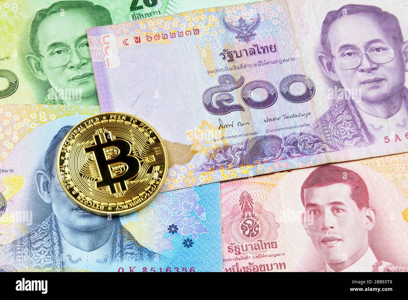 Close-up on a golden Bitcoin coin on top of a stack of Thai Baht banknotes. Stock Photo