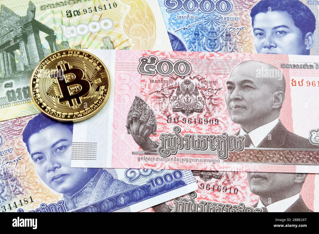 Close-up on a golden Bitcoin coin on top of a stack of Cambodian riel banknotes. Stock Photo