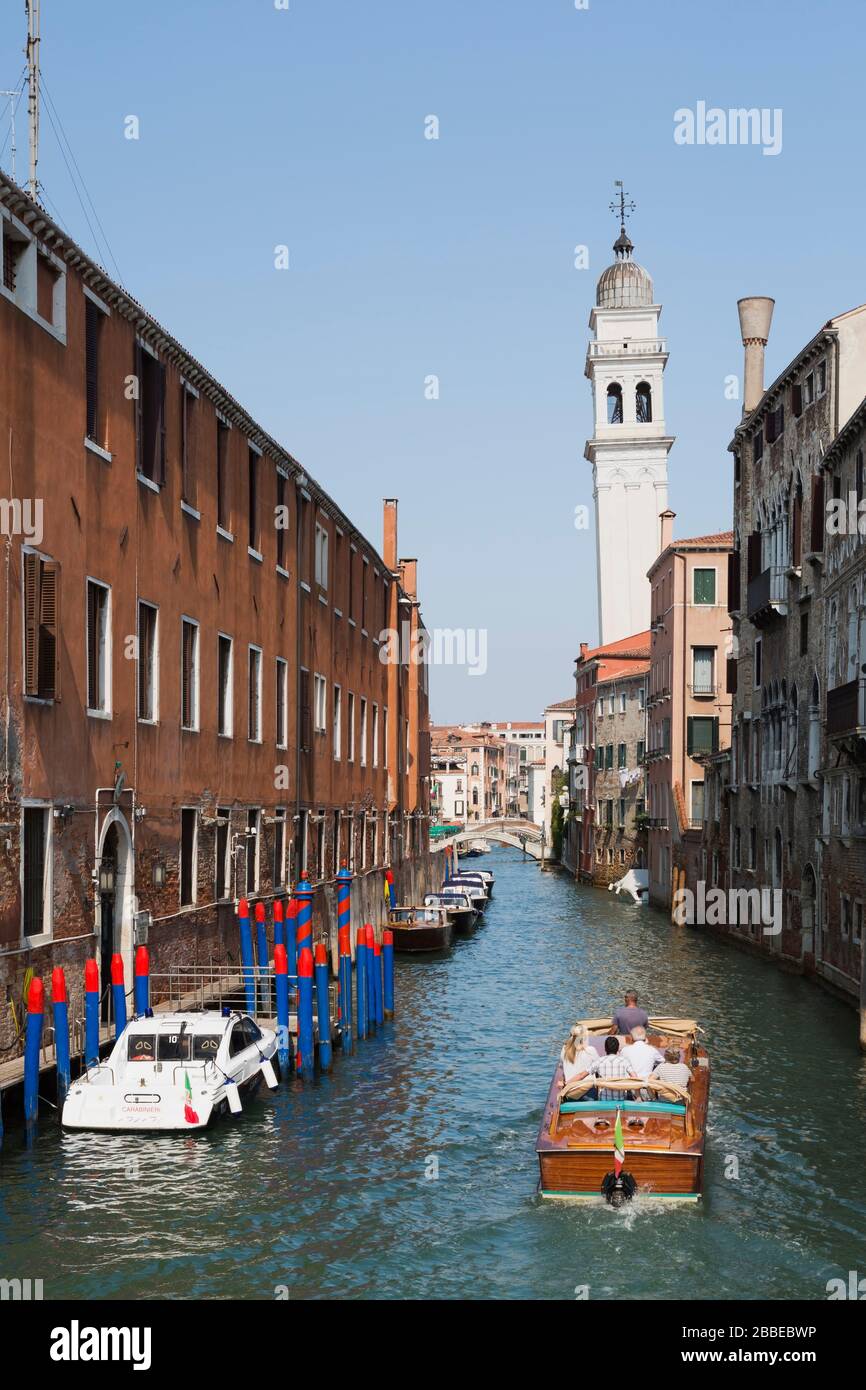 Water taxi and moored boats on narrow canal and old architectural style residential buildings, leaning church bell tower, San Marco, Venice, Veneto, Italy Stock Photo