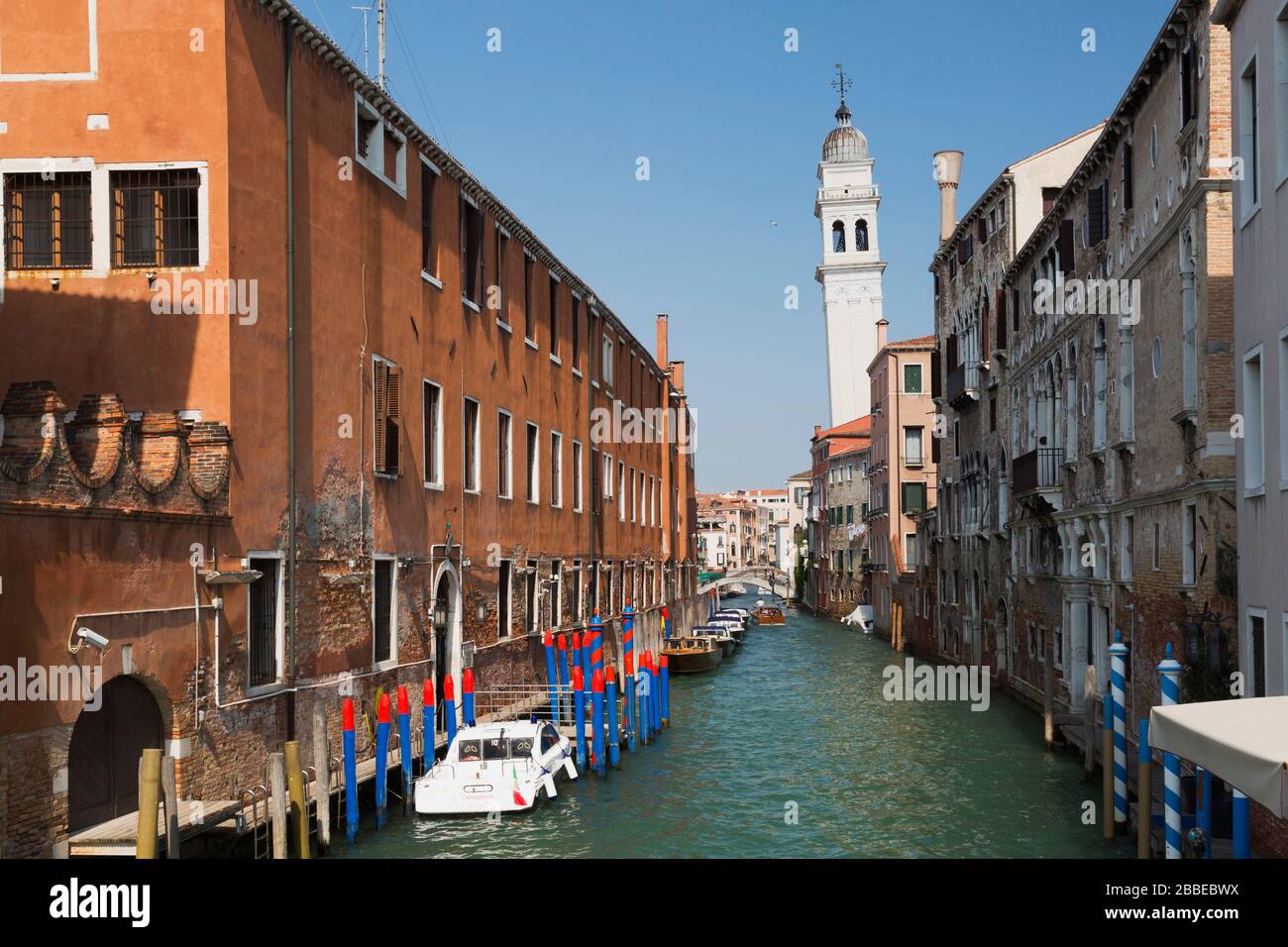 Moored boats and water taxi on narrow canal and old architectural style residential buildings, leaning church bell tower, San Marco, Venice, Veneto, Italy Stock Photo