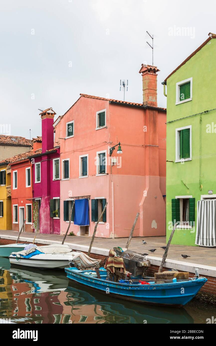 Moored boats in canal lined with green, pink, purple, red and yellow stucco houses decorated with curtains over entrance doors, Burano Island, Venetian Lagoon, Venice, Veneto, Italy Stock Photo