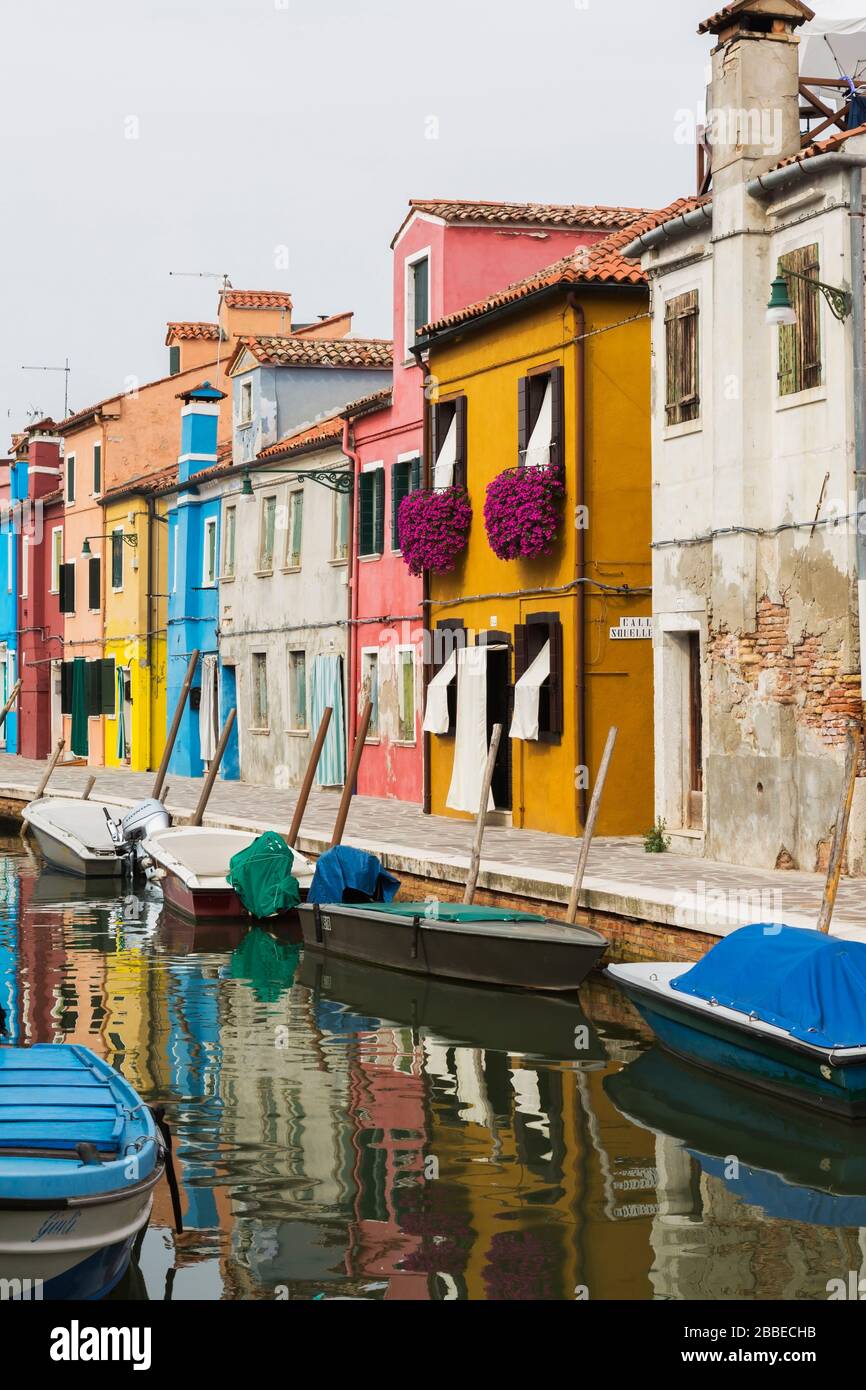 Moored boats on canal lined with colourful stucco houses decorated with striped curtains over entrance doors and windows, Burano Island, Venetian Lagoon, Venice, Veneto, Italy Stock Photo