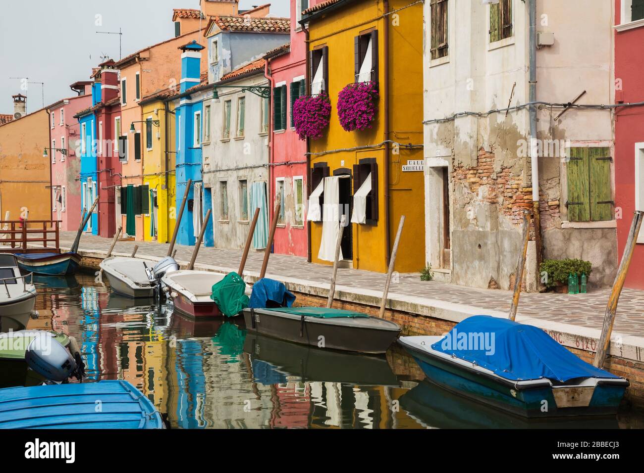 Moored boats on canal lined with colourful stucco houses decorated with striped curtains over entrance doors and windows, Burano Island, Venetian Lagoon, Venice, Veneto, Italy Stock Photo