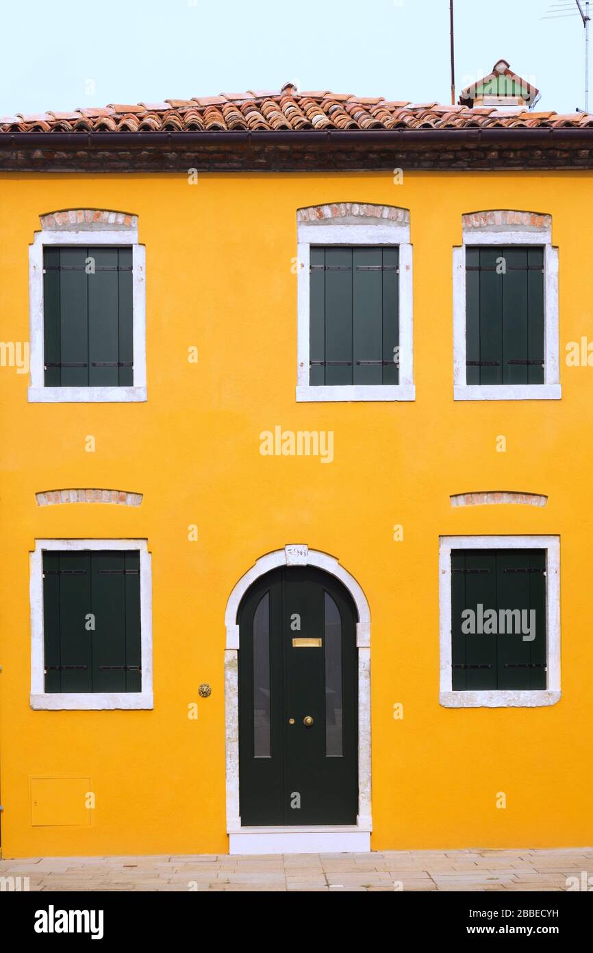 Yellow stucco house facade with brown arched entrance door and  shuttered windows, Burano Island, Venetian Lagoon, Venice, Veneto, Italy Stock Photo