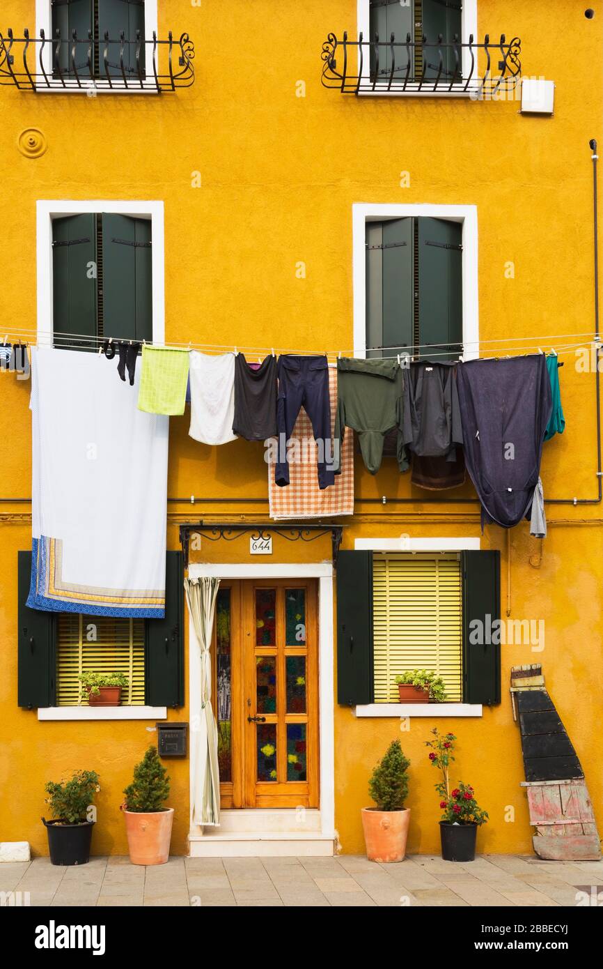 Yellow stucco house facade with doorsteps and washed clothes on clothesline, Burano Island, Venetian Lagoon, Venice, Veneto, Italy Stock Photo