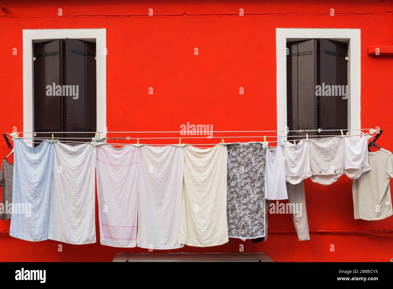 Red stucco house facade with washed clothes on clothesline, Burano Island, Venetian Lagoon, Venice, Veneto, Italy Stock Photo