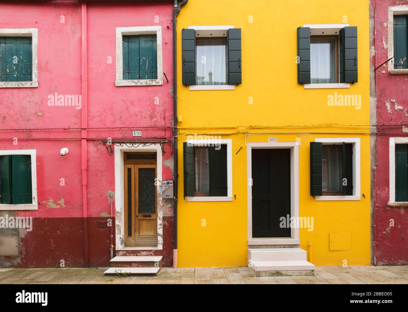 Pink and yellow stucco house facades with doorsteps and green wooden storm shutters on windows, Burano Island, Venetian Lagoon, Venice, Veneto, Italy Stock Photo
