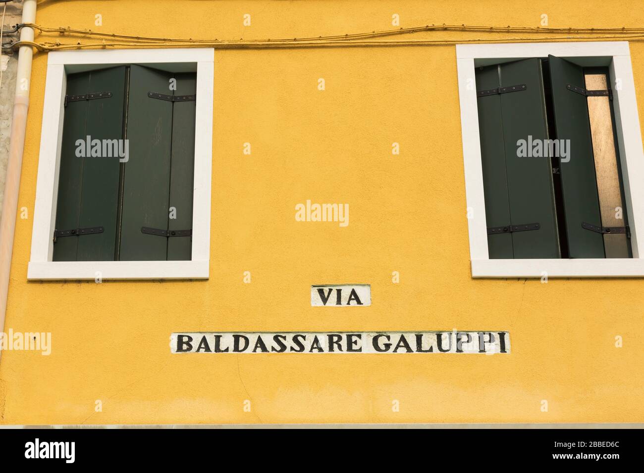 Via Baldassare Galuppi inscription on yellow stucco exterior house wall with green wooden shutters, Piazza Baldassare Galuppi, Burano Island, Venetian Lagoon, Venice, Veneto, Italy Stock Photo