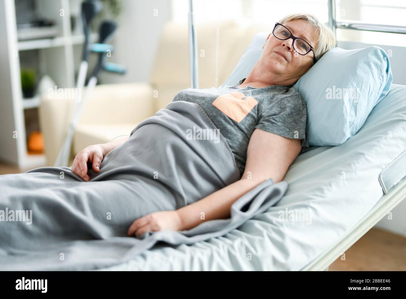 Elderly age woman laying on a bed in a nursing home covered with a