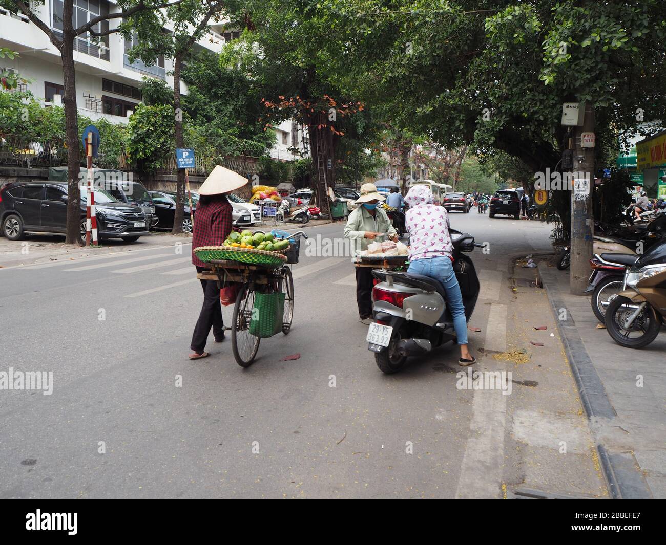 Women on bikes selling fresh fruit and other foods wearing conical hats and masks for protection during the coronavirus pandemic, Hanoi, Vietnam Stock Photo
