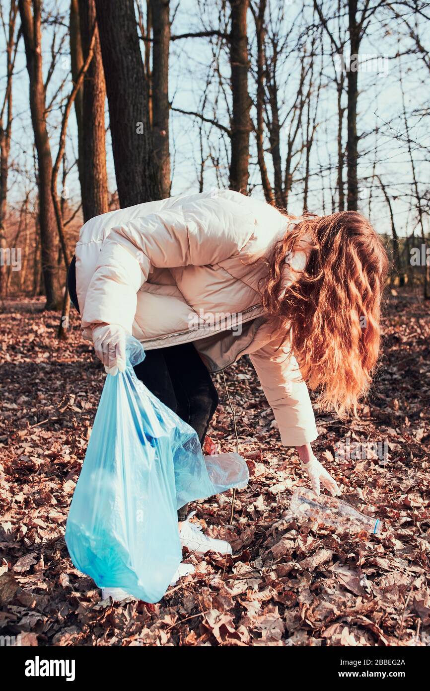Young woman cleaning up a forest. Volunteer picking plastic waste to bags. Concept of plastic pollution and too many plastic waste. Environmental issu Stock Photo