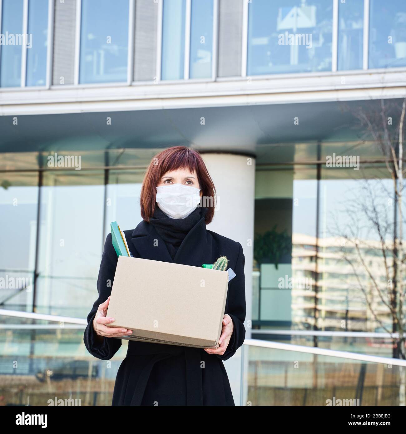 Concept of job loss due to the COVID-19 virus pandemic. Woman in mask lost job because of coronavirus. Female with box of his things against backgroun Stock Photo
