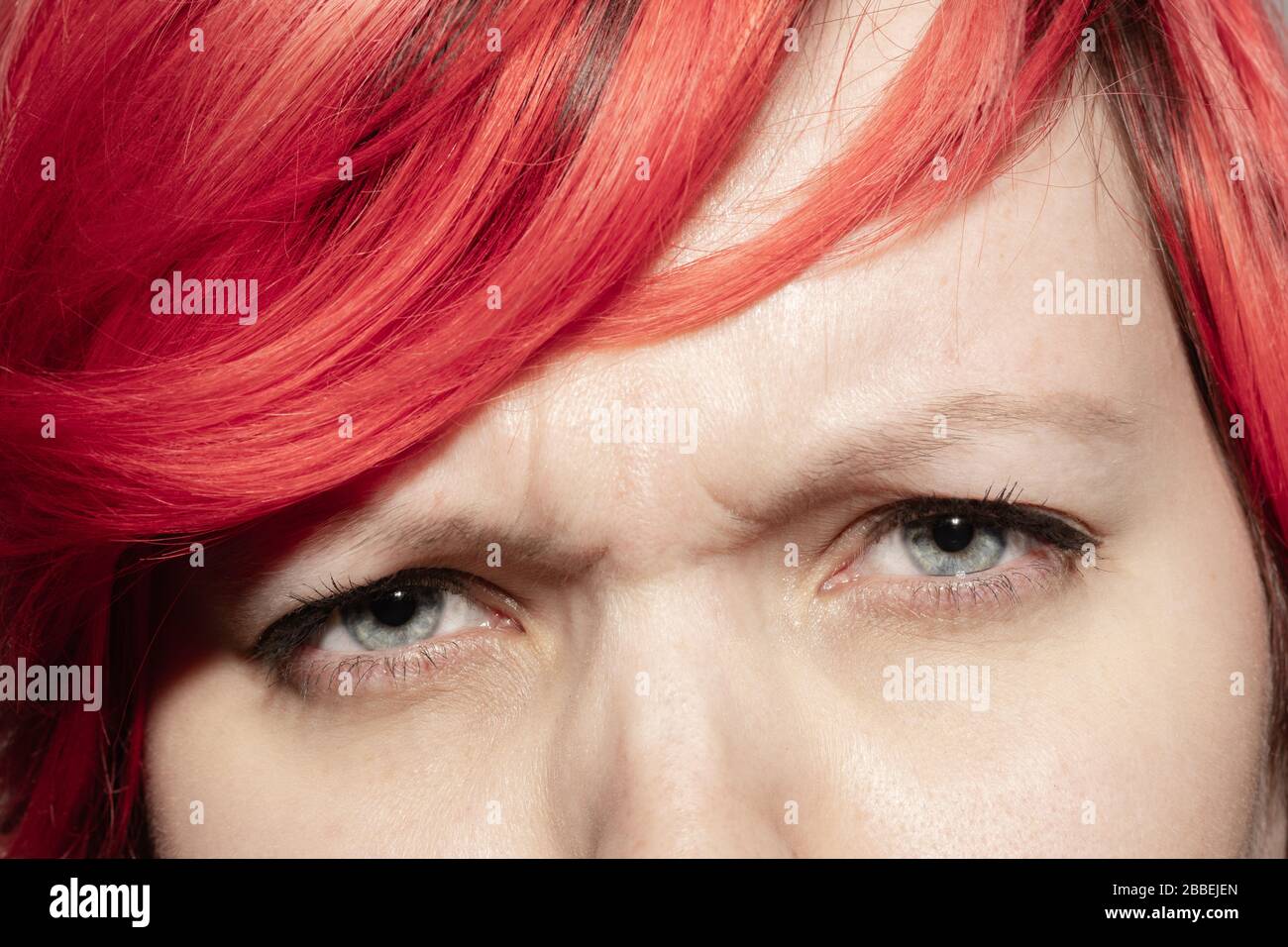 Angry. Close up of face of beautiful caucasian young woman, focus on eyes. Human emotions, facial expression, cosmetology, body and skin care concept. Well kept cheeks, narutal make up. Wellbeing. Stock Photo