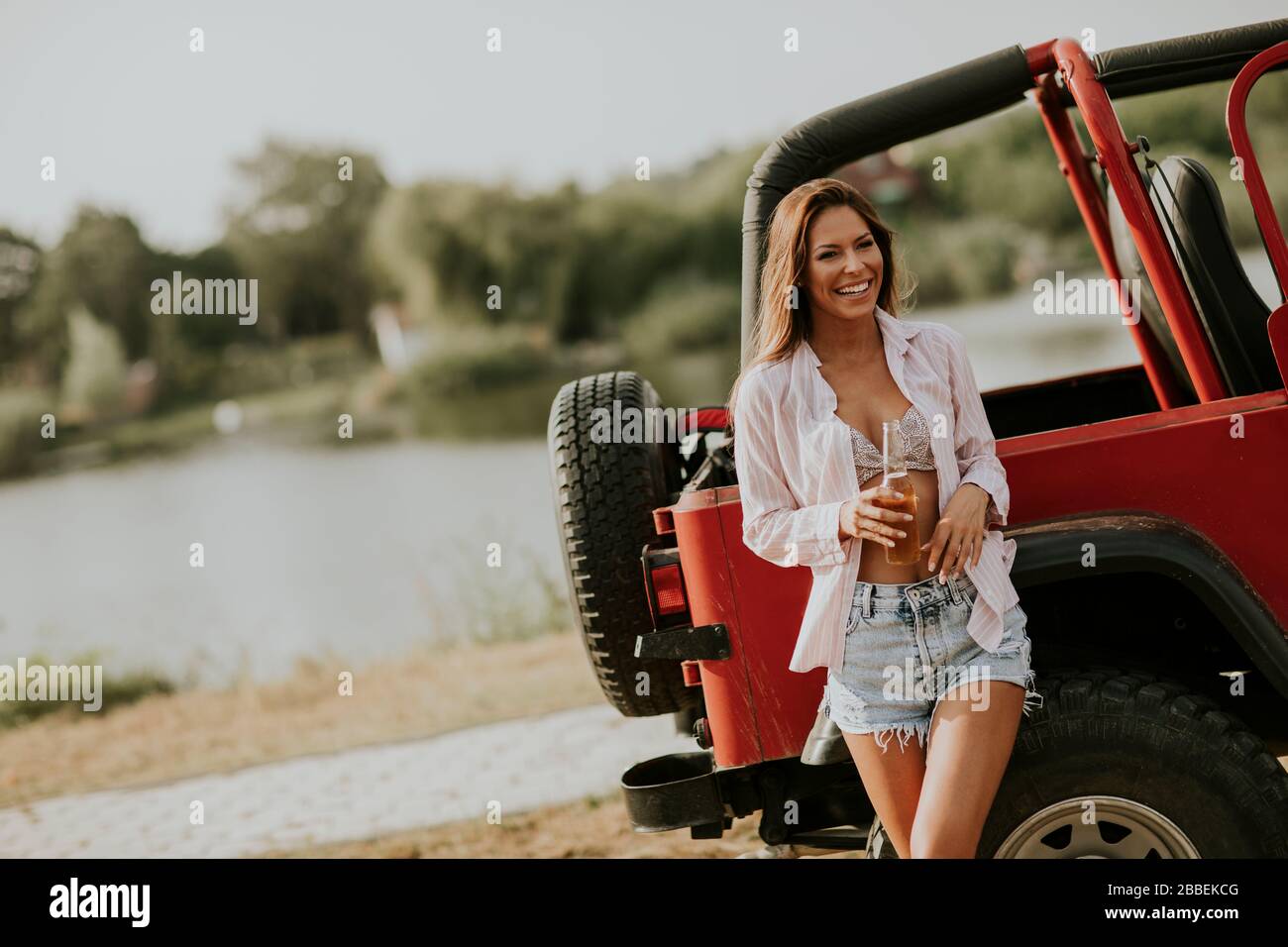 Pretty young woman relaxing by the car on the lakeside Stock Photo
