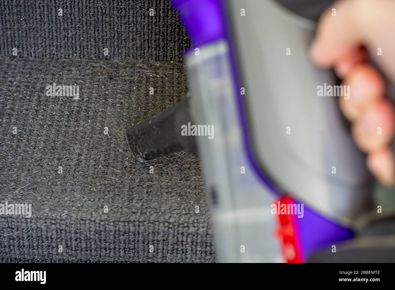 Hand holding a handheld vacuum cleaner to remove dirt from the stairs covered with carpet. Stock Photo