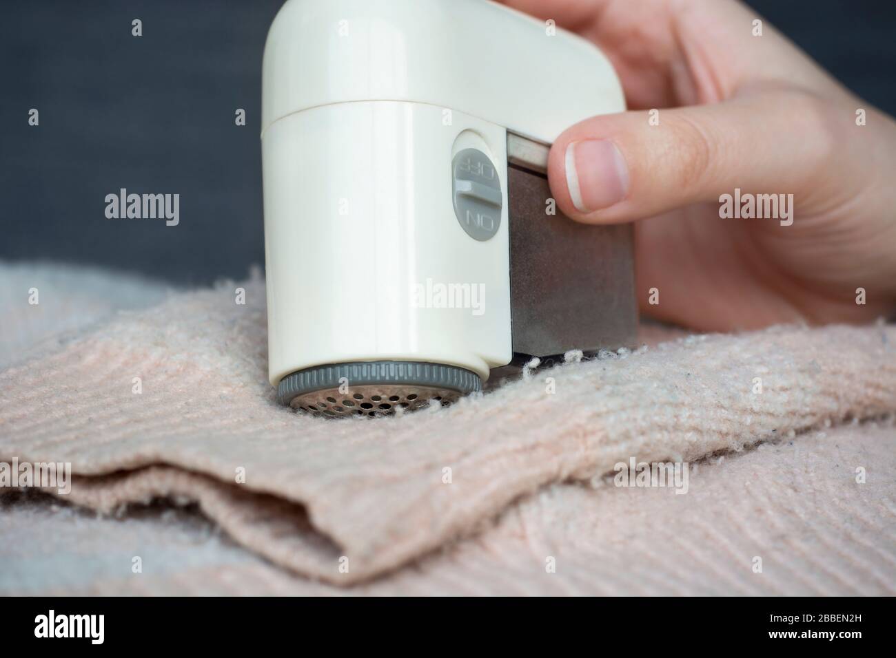 Pilled sweater. Woman hand using handheld electric fabric shaver fuzz remover device machine for removing fuzz, lint and pills (pilling) on clothes Stock Photo