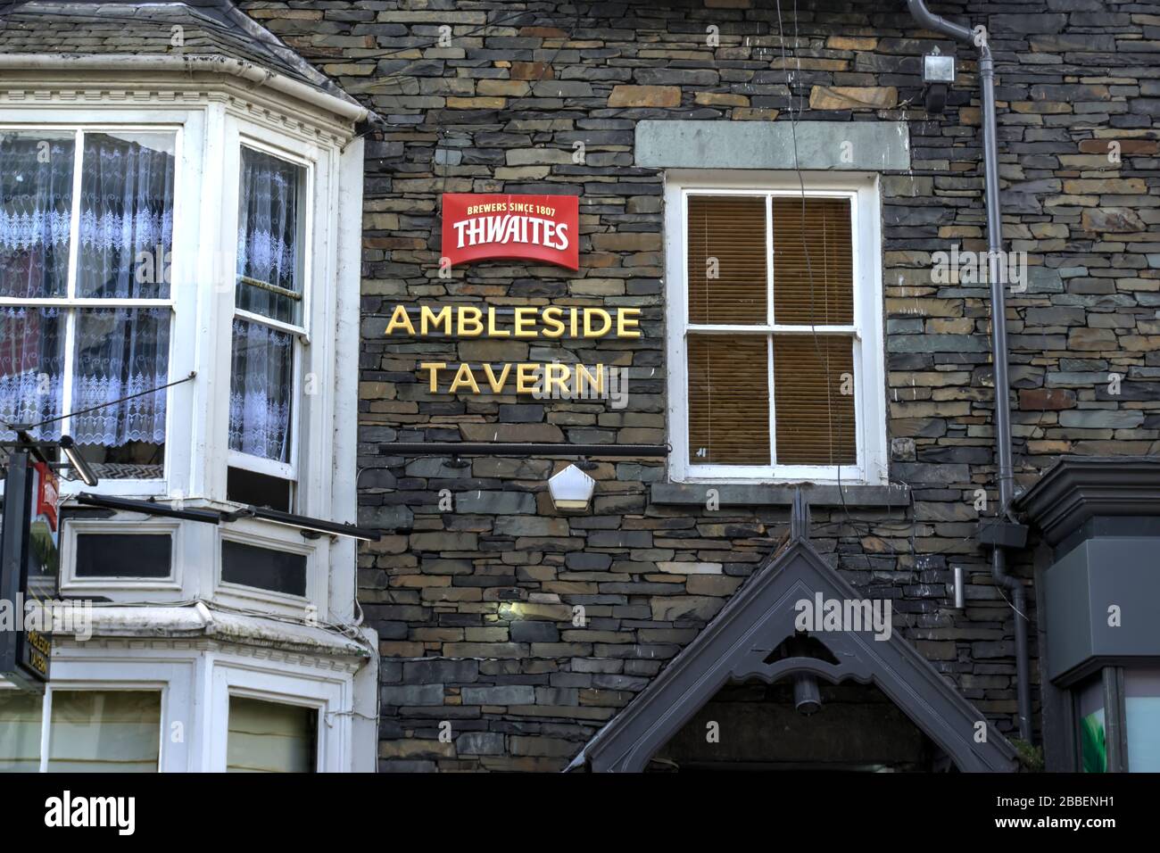 Ambleside, Cumbria, United Kingdom - May 16, 2019: Signage on drystone wall indicating Thwaites brewery and Ambleside Tavern Stock Photo