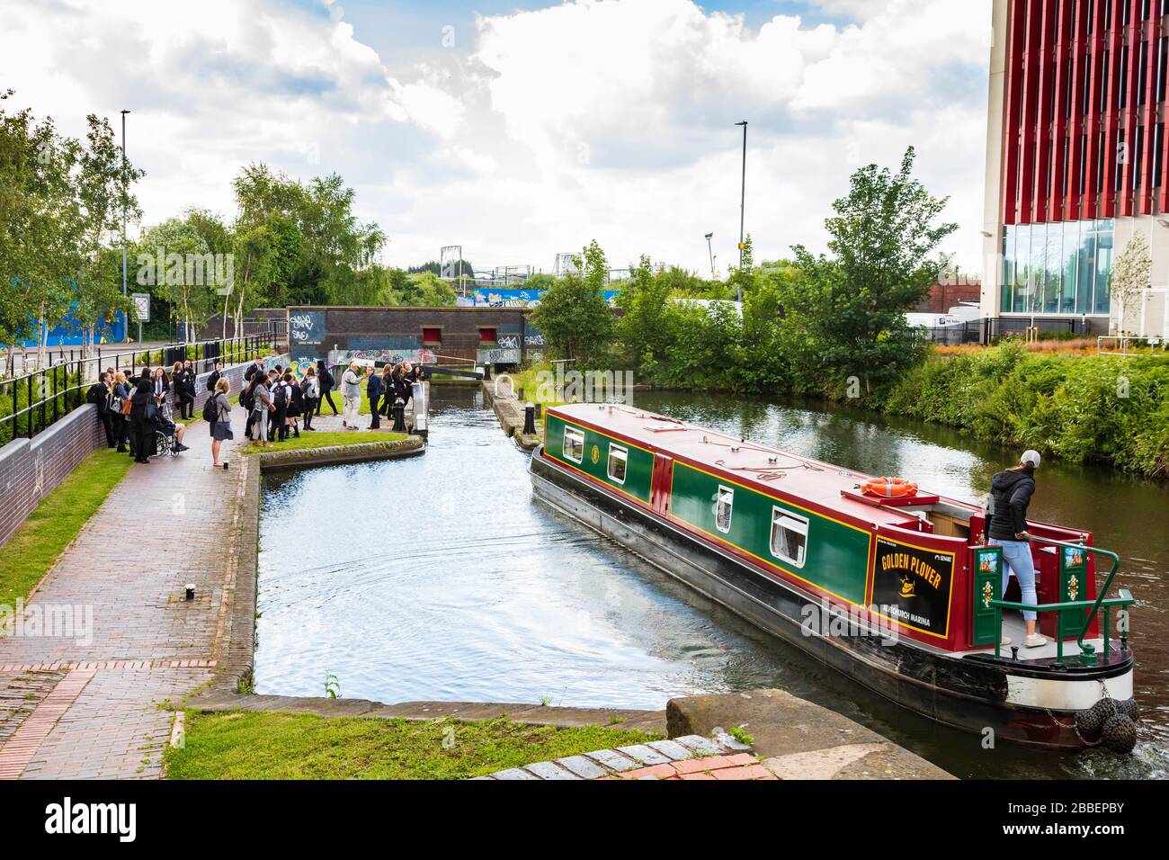 A group of teenage school children have a lesson on the Canalside by Curzon Street tunnel, a narrowboat negotiates the lock. Birmingham, UK Stock Photo
