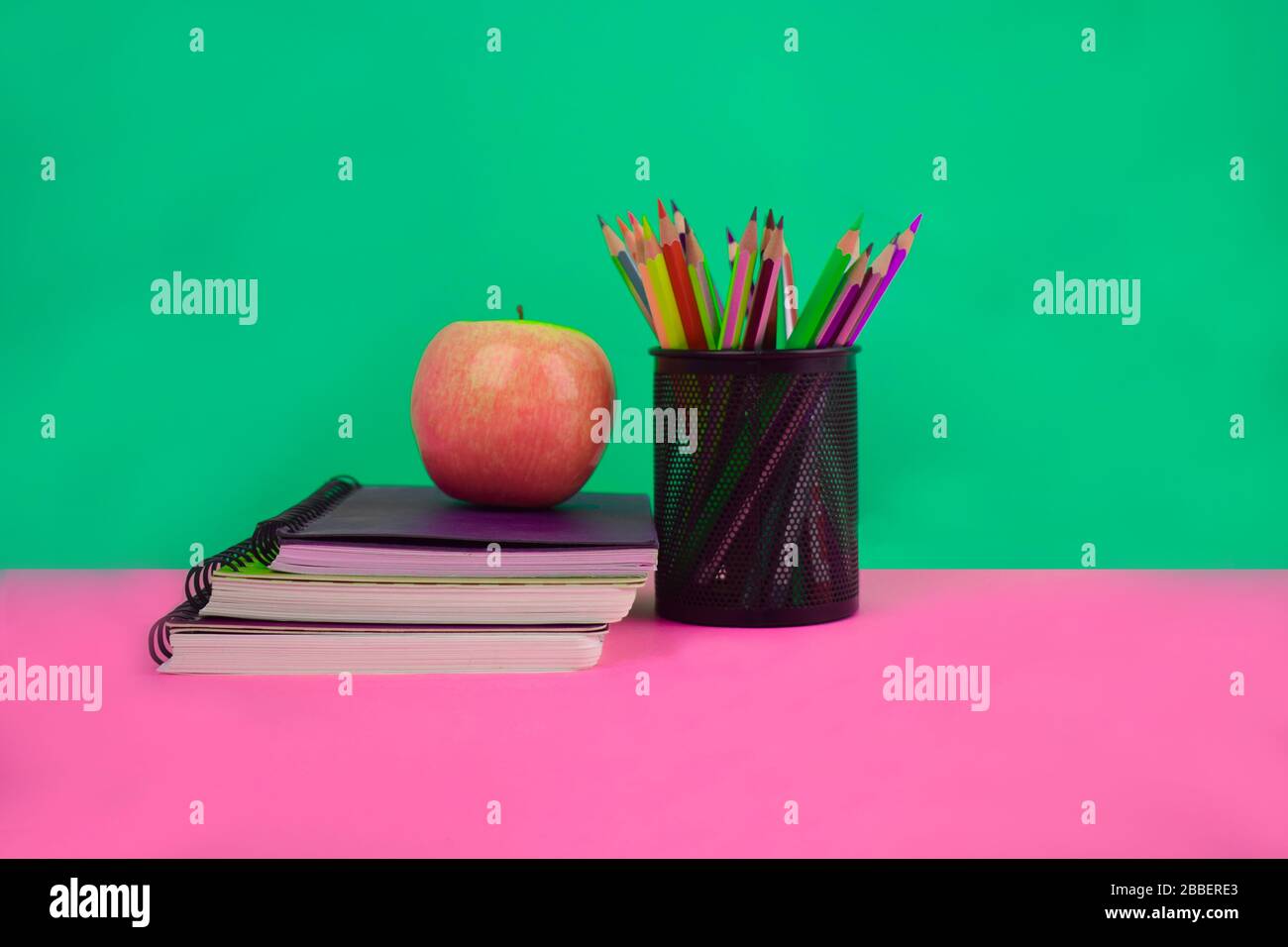 Three diaries,an apple and a jar full of different colored pencil crayons stacked together before a paper background Stock Photo
