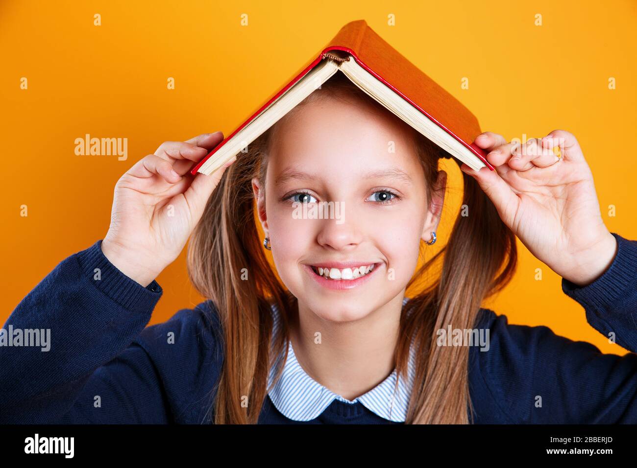 cute little school girl holding book over head like roof on yellow