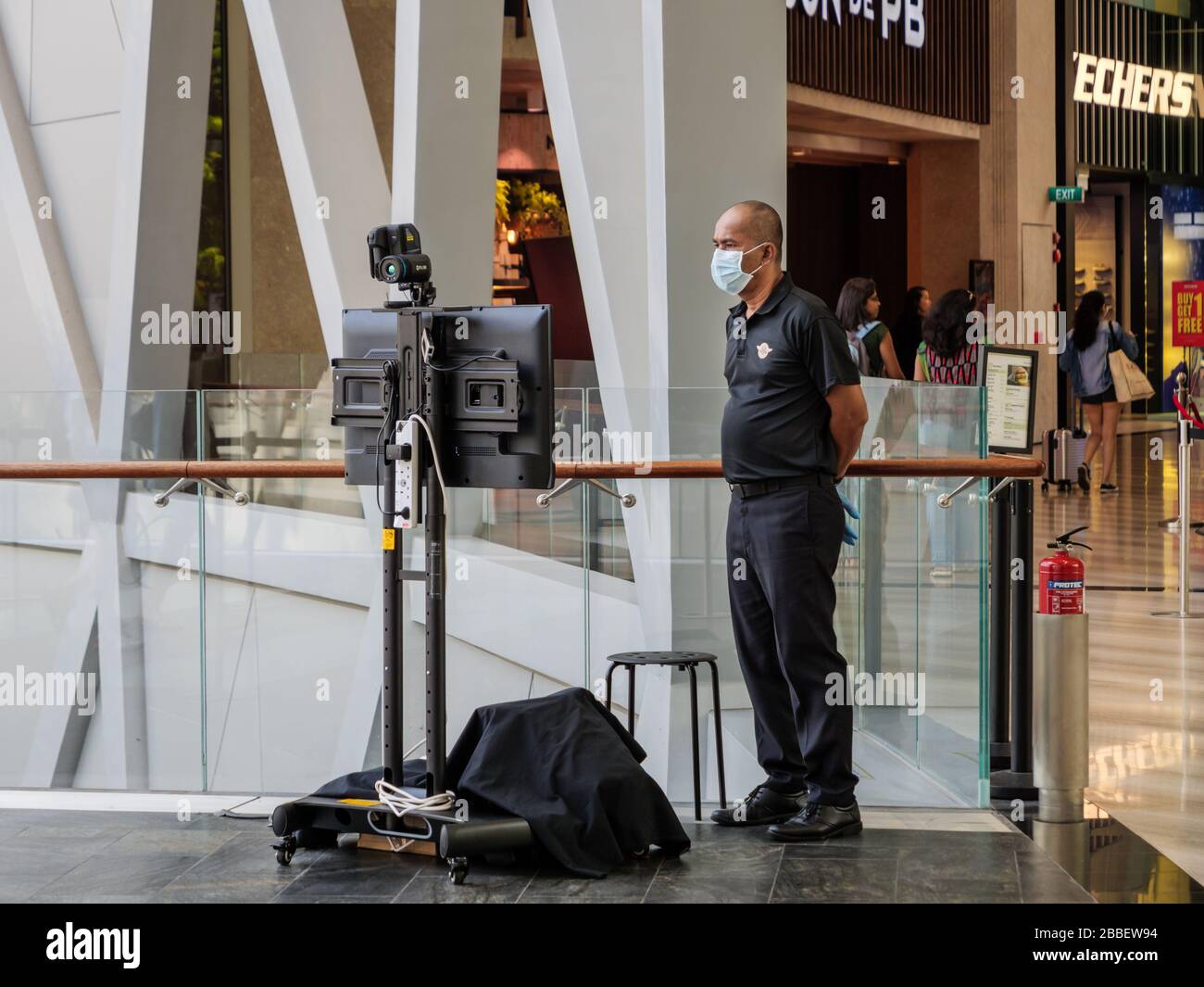 SINGAPORE – 23 MAR 2020 – Security guard wearing a mask operates a FLIR thermal imaging temperature scanner / camera scanner at Jewel Mall, Changi Air Stock Photo