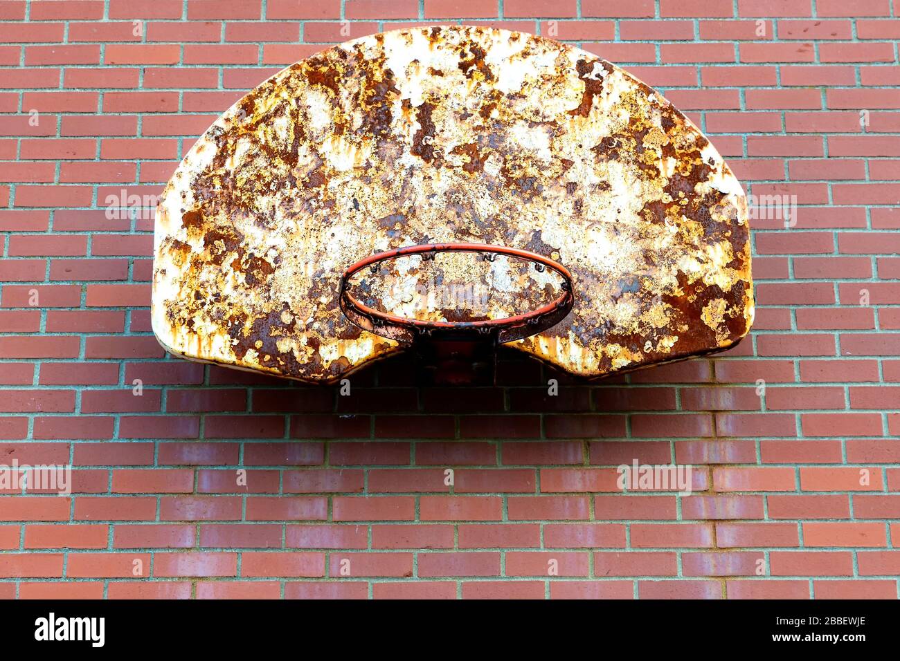 An old basketball hoop mounted outdoors on a brick wall. The netting is gone, and the backboard is dirty and rusty. Room for text. Stock Photo