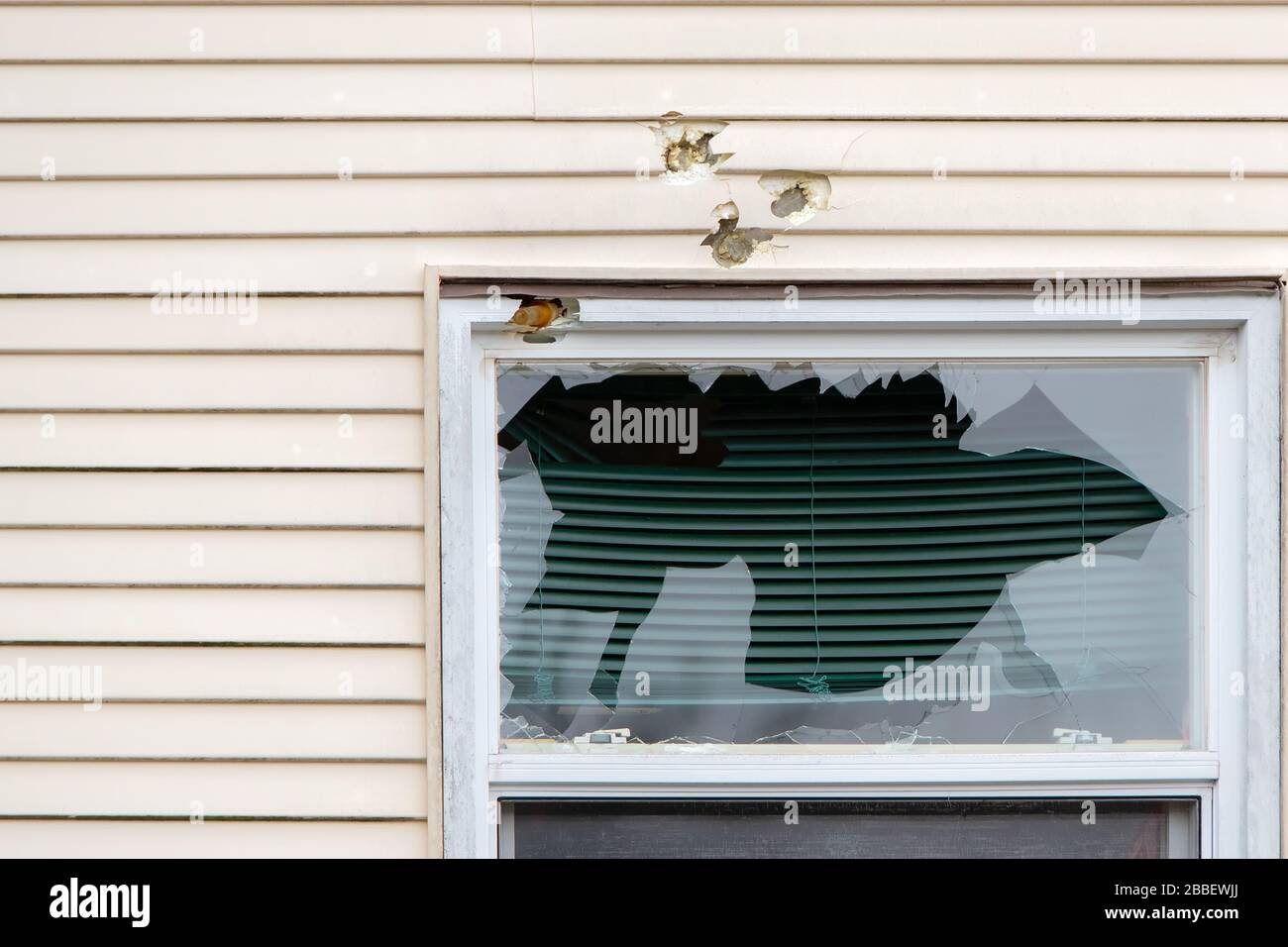 A broken window with holes above it. The holes were created by baton and tear gas shots fired by police. A baton ground is stuck in the window frame. Stock Photo